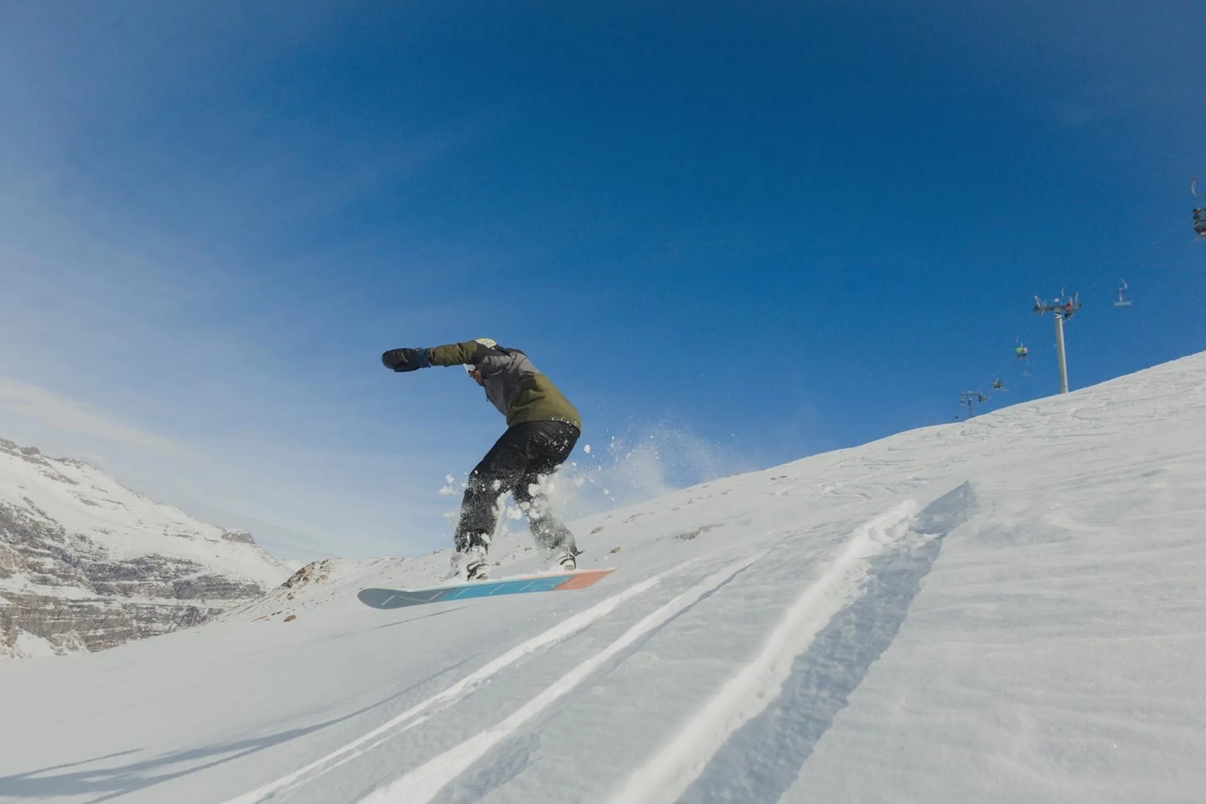 Snowboarder descendo uma pista de neve sob céu azul, em foto do acervo de Ski Day da Geminis Tours.